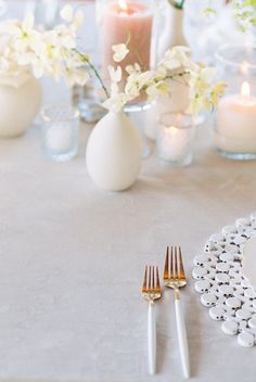 the table is set with silverware and white flowers in vases, candles, and napkins