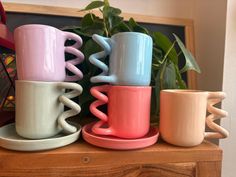 three coffee mugs are stacked on top of each other in front of a potted plant