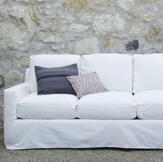 a white couch sitting next to a stone wall with two pillows on top of it