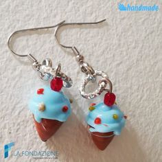 two blue cupcakes are hanging from silver earwires on a white surface