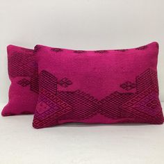 two bright pink pillows on a white surface, one has an intricate design and the other is