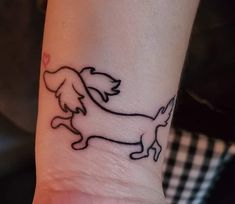 a small black and white dog tattoo on the left inner wrist, with an outline of a dachshund running