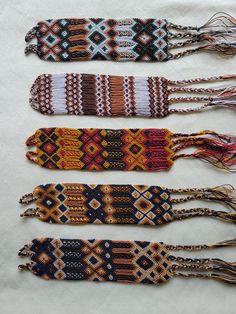 four bracelets are lined up on a white tablecloth with tassels hanging from them