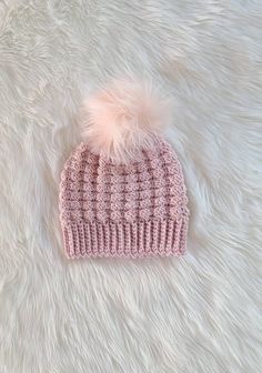 a pink knitted hat with a fuzzy pom - pom on the top