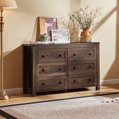 a wooden dresser sitting on top of a hard wood floor next to a lamp and pictures