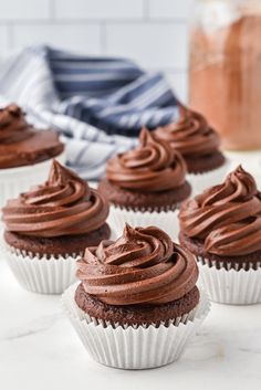 chocolate cupcakes with frosting sitting on a white table next to a jar of peanut butter