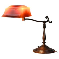 an old fashioned table lamp with a red shade on it's side and a metal base