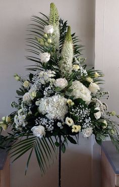 white flowers and greenery are arranged on a tall metal stand in front of a wall