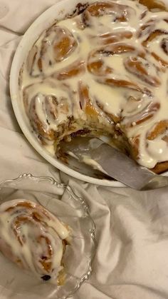 a white plate topped with a dessert covered in frosting and cinnamon rolls next to a glass bowl