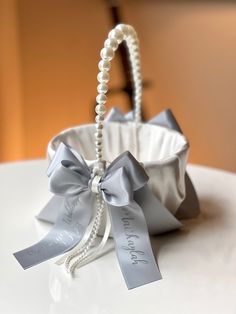 a white basket with pearls and ribbon tied around the handle on top of a table