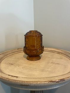 an old glass vase sitting on top of a wooden table next to a white wall