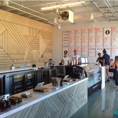 people are standing in front of the counter at an open air coffee shop, with menus on the wall behind them