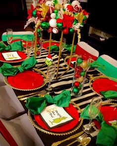 the table is set for christmas dinner with red and green place mats, silverware, candy canes, gold rimmed glasses