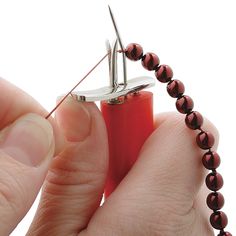 a person is holding a bead with a pair of scissors in their hand and the beads are red