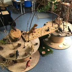 an assortment of fake animals on display in a museum setting with trees, rocks and plants