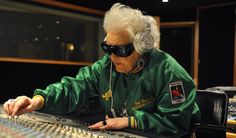 an old man wearing headphones sitting at a mixing desk