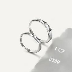 two silver rings sitting next to each other on top of a white surface with the words i love you