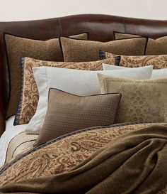 a bed covered in pillows and blankets with a brown headboard on top of it