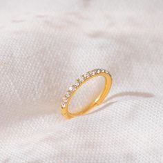 a gold ring with small white stones on it sitting on a white fabric background in close up view