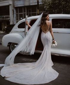 a woman in a wedding dress standing next to an old car