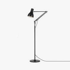 a black floor lamp on a white background with the light turned on and plugged in