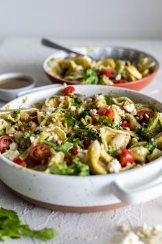 two bowls filled with pasta and veggies on top of a white tablecloth