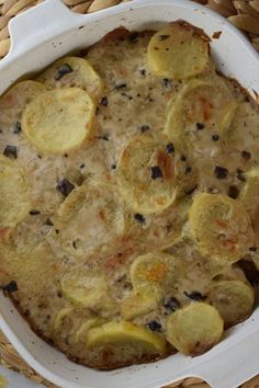 a casserole dish with potatoes and black olives in it on a wicker place mat