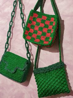 two crocheted purses hanging from chains on a pink surface, one is green and the other is red