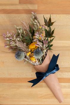 a bouquet of wildflowers wrapped in blue ribbon on a wooden surface with wood flooring