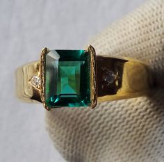 an emerald colored ring with two diamonds on the band and in gold plated setting