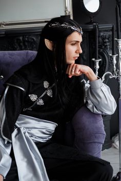 a woman with long hair sitting on a purple chair wearing a black and silver outfit