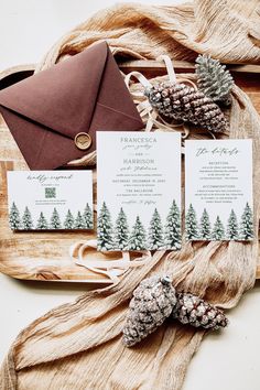 the wedding stationery is laid out on a wooden tray with pine cones and an envelope