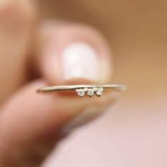 a woman's hand holding a tiny gold ring with three small diamonds on it