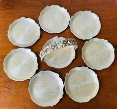 six white plates sitting on top of a wooden table next to a silver bowl and spoon