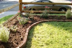 a car parked behind a wooden fence in the grass next to some flowers and bushes