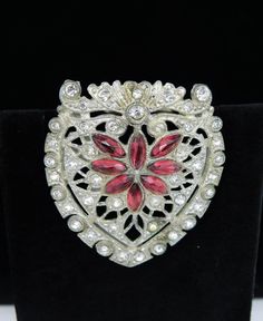 This wonderful 1950's Art Deco Pot Metal Dress Clip was an amazing find and would be a wonderful addition to anyone's dress clip collection.  Created in molded pot metal/white metal, the design is almost that of a heart shaped shield, and it includes clear red rhinestone navettes to help complete that look.  The rest of the piece is fully decked out in strategically placed clear rhinestone chatons to compliment the silver metal flourishes and studs of the design. This clip measures 1 3/4 inches 1950s Art, Metal Dress, Dress Clips, Dress Clip, Red Rhinestone, Shoe Clips, Purple Lilac, Art Deco Style, Gorgeous Earrings