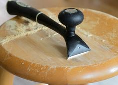 a small wooden stool with a black handle on it's top and a brush sticking out of the seat