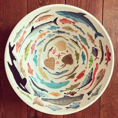 a bowl with fish painted on it sitting on a wooden floor next to a wall