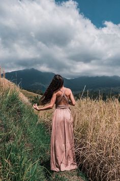 a woman standing in tall grass with her back to the camera and looking at mountains