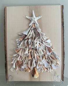 a christmas tree made out of seashells on a wooden board with a starfish hanging from the top