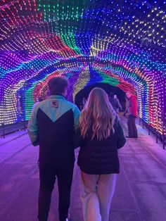 a man and woman walking through a tunnel covered in lights