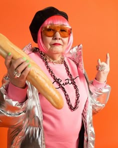 a woman in pink is holding a large hot dog and wearing sunglasses on an orange background