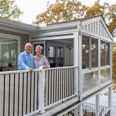 an older couple standing on the balcony of their house next to a lake or river