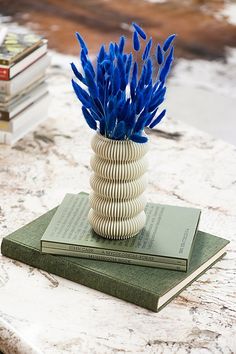 blue flowers in a white vase sitting on top of a book next to a stack of books