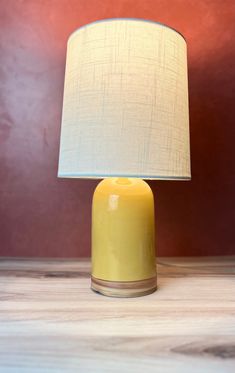 a yellow table lamp sitting on top of a wooden table next to a red wall