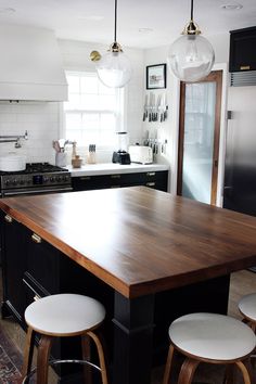 a kitchen island with stools in front of it and lights hanging from the ceiling