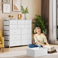 a woman sitting on the floor in front of a white chest of drawers next to a yellow chair