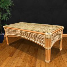 a wicker coffee table sitting on top of a wooden floor next to a potted plant