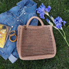 a purse and some blue flowers are laying on the grass next to a pair of jeans