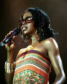 a woman in a colorful dress holding a microphone and singing into a mic on stage